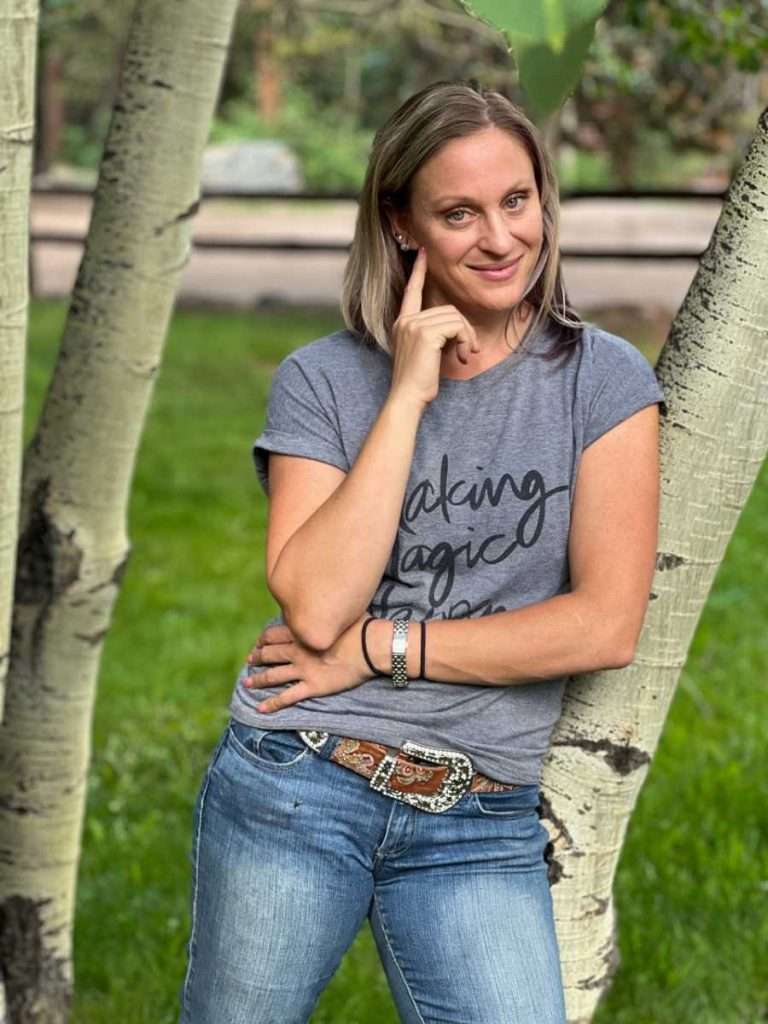 A woman leaning against a tree wearing a gray t-shirt.